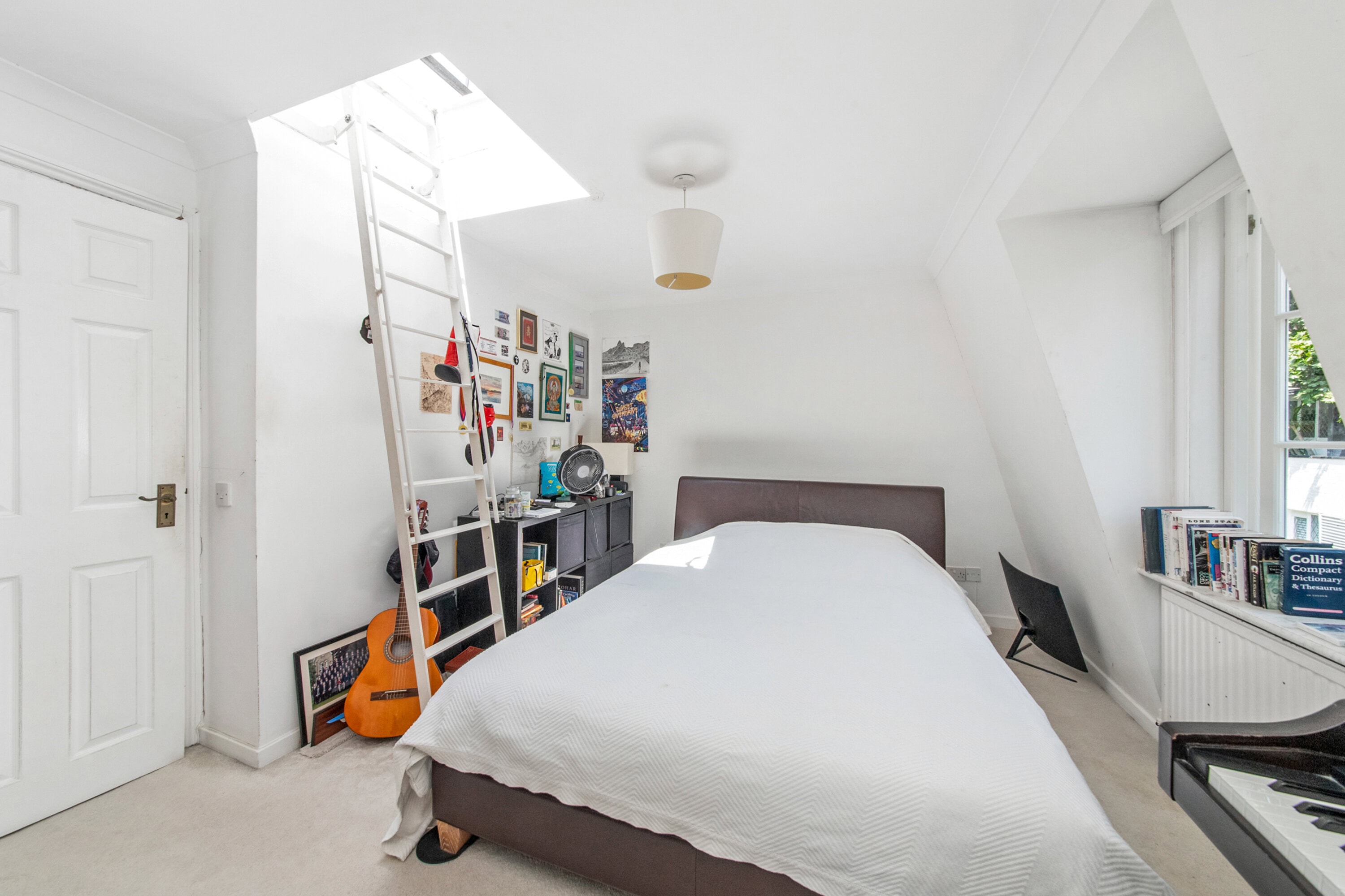 Bright bedroom with sloped ceiling, guitar, and artwork on the wall.