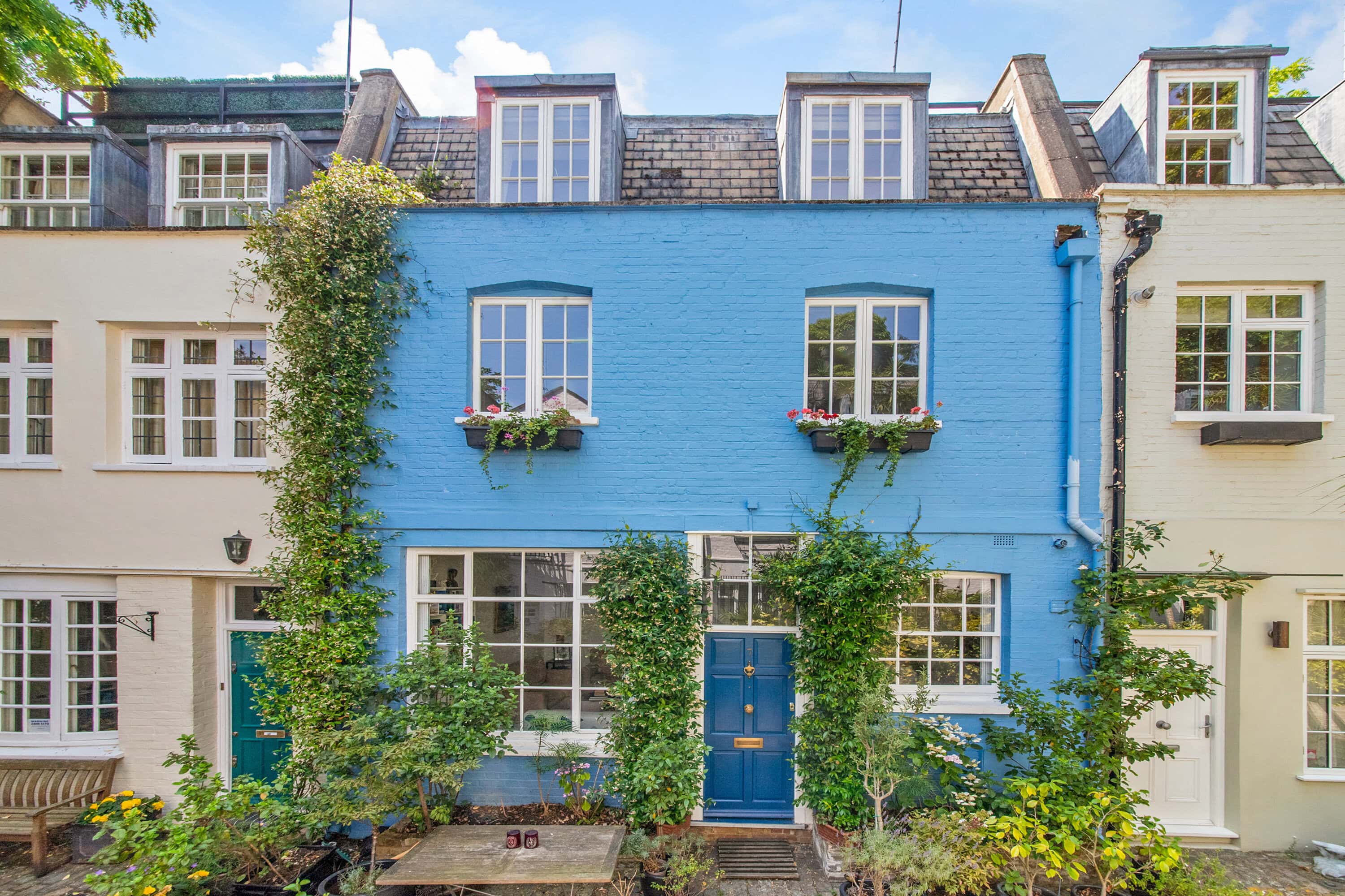 Colourful mews home for sale with vibrant blue facade and lush greenery.