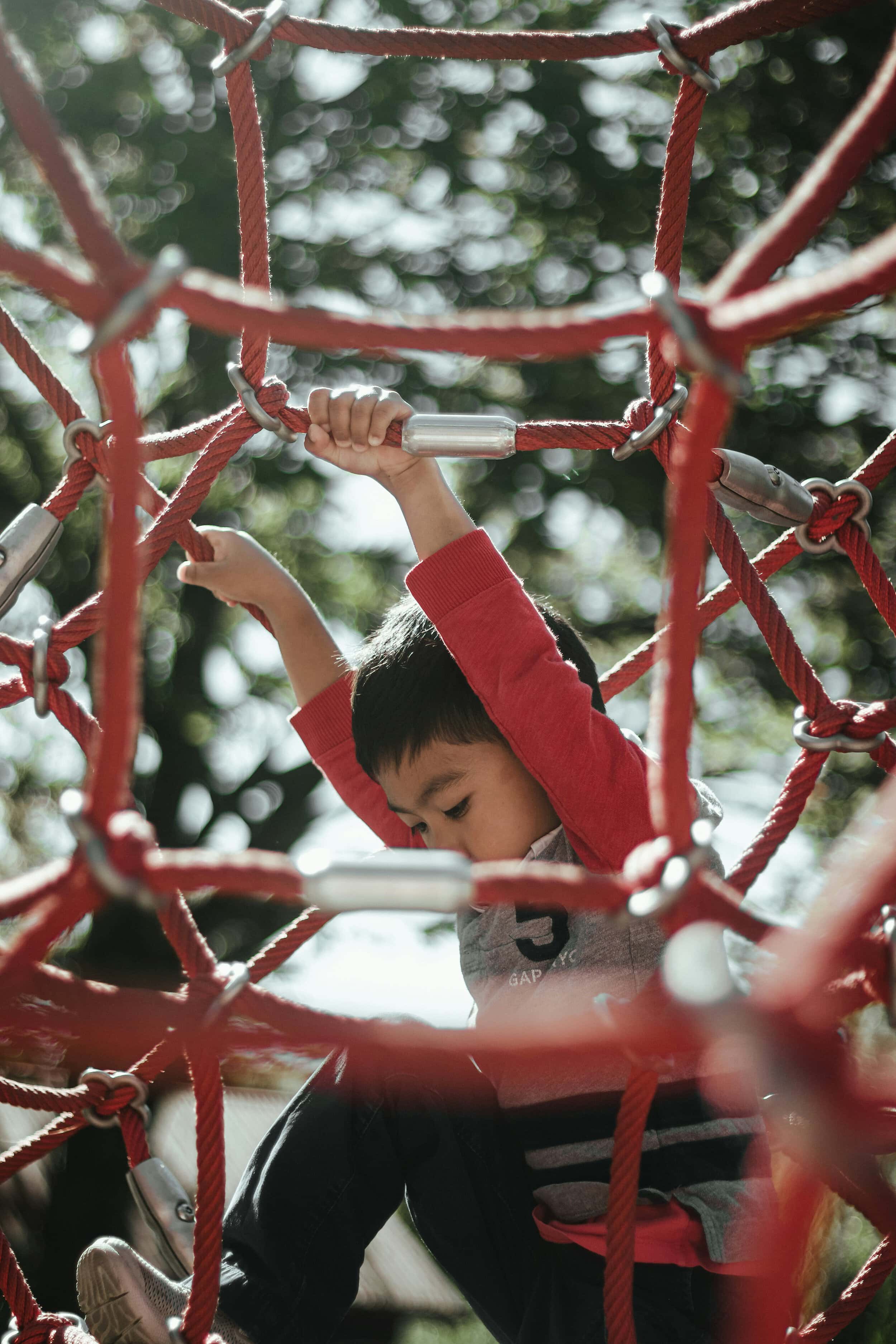 Young boy climbing on red playground climbing frame in park.
