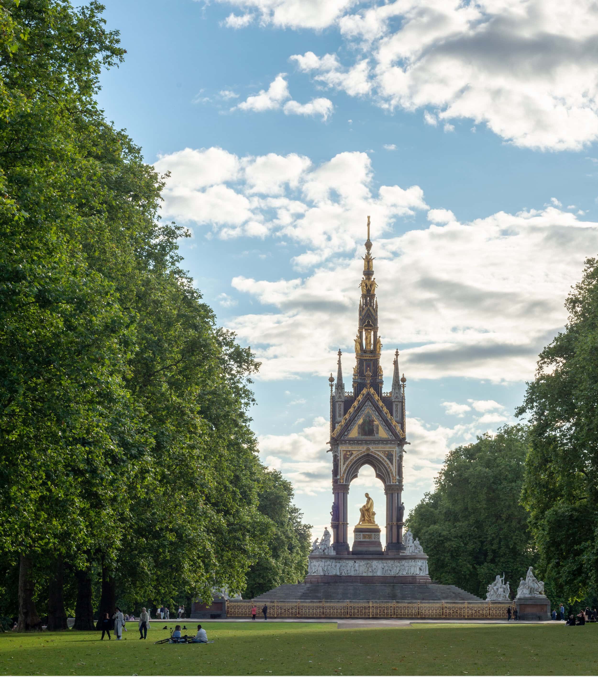 Albert Memorial in Kensington Gardens with lush green trees and blue sky.