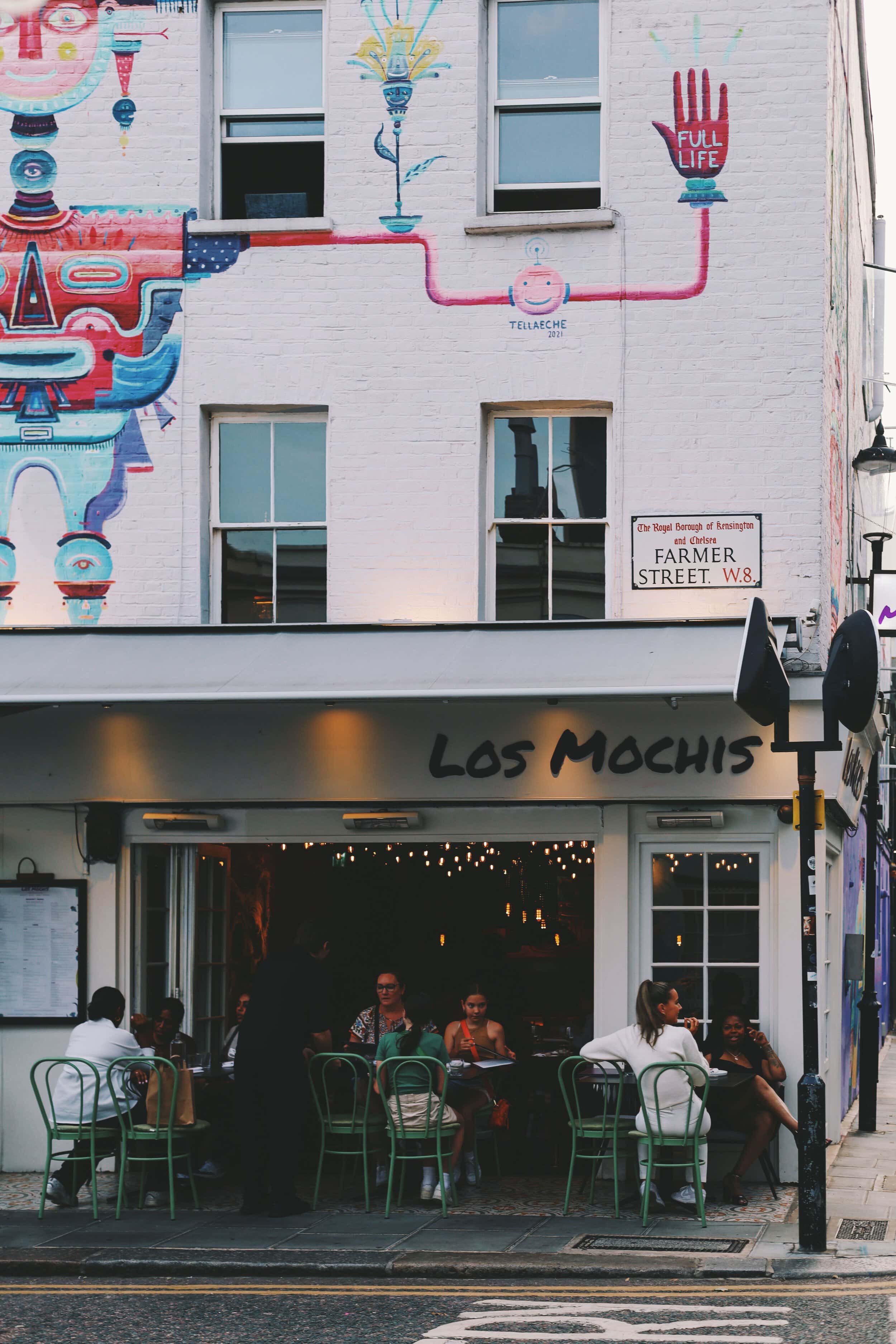 Charming cafe scene in Notting Hill with outdoor seating and vibrant street art, easy to access to those who want to rent in Notting Hill
