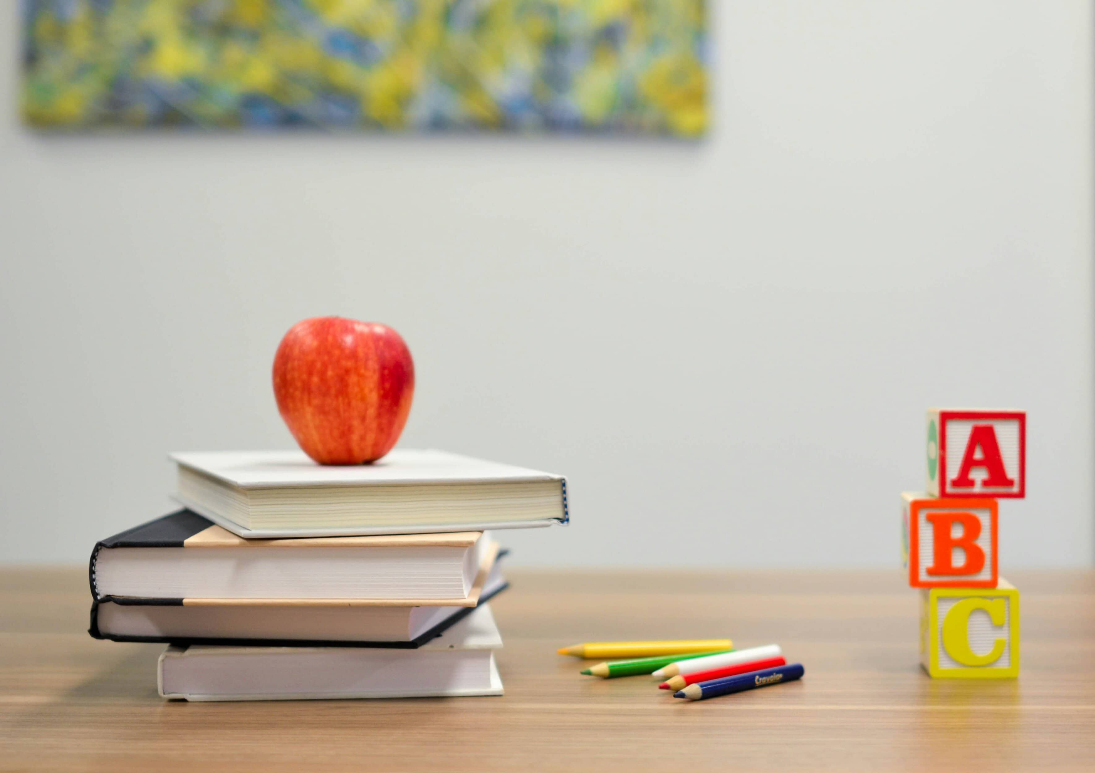 Stack of books with an apple and colourful alphabet blocks on a desk.