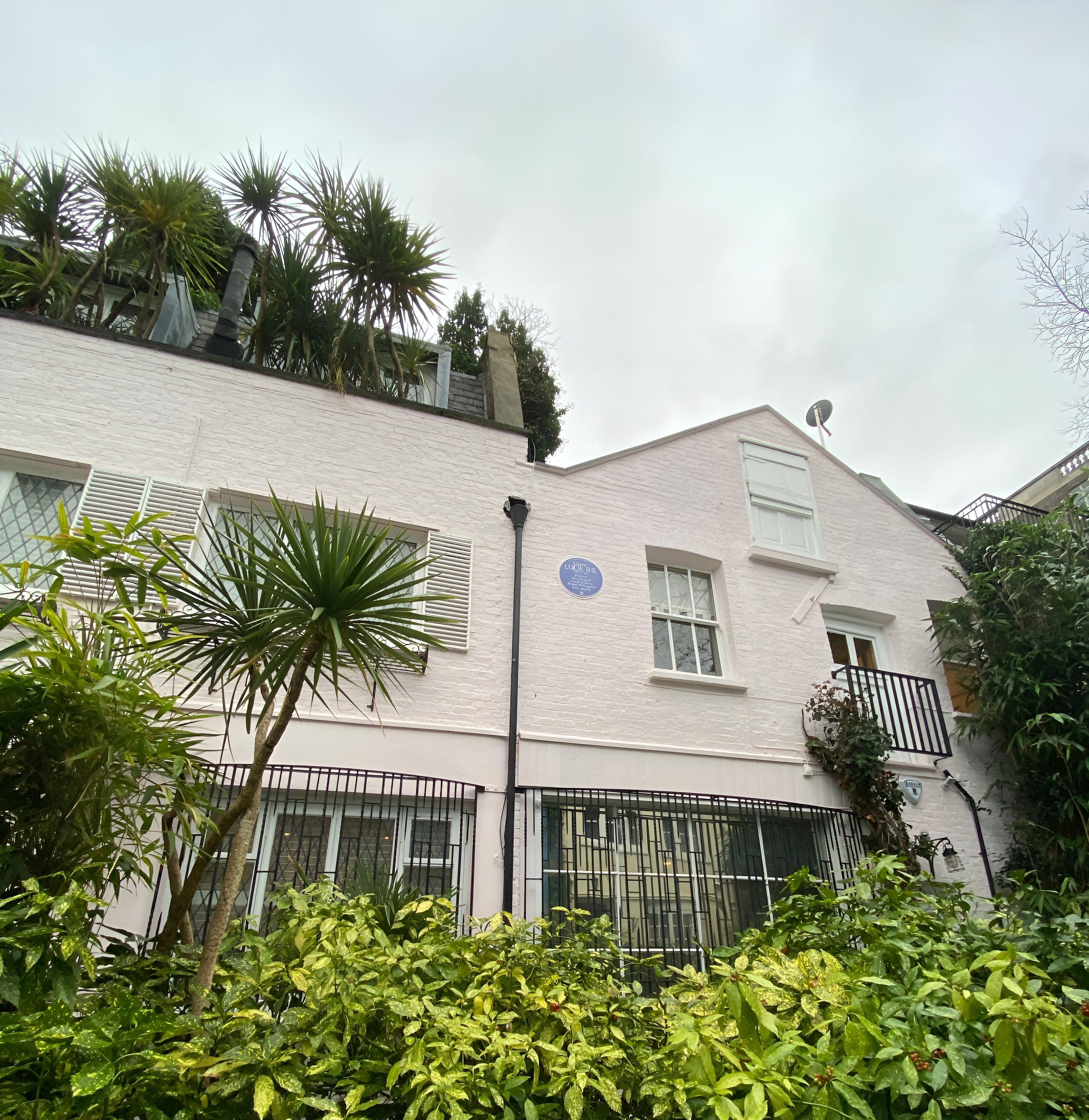 White mews house with plaques on its wall with lush garden and balcony in London.