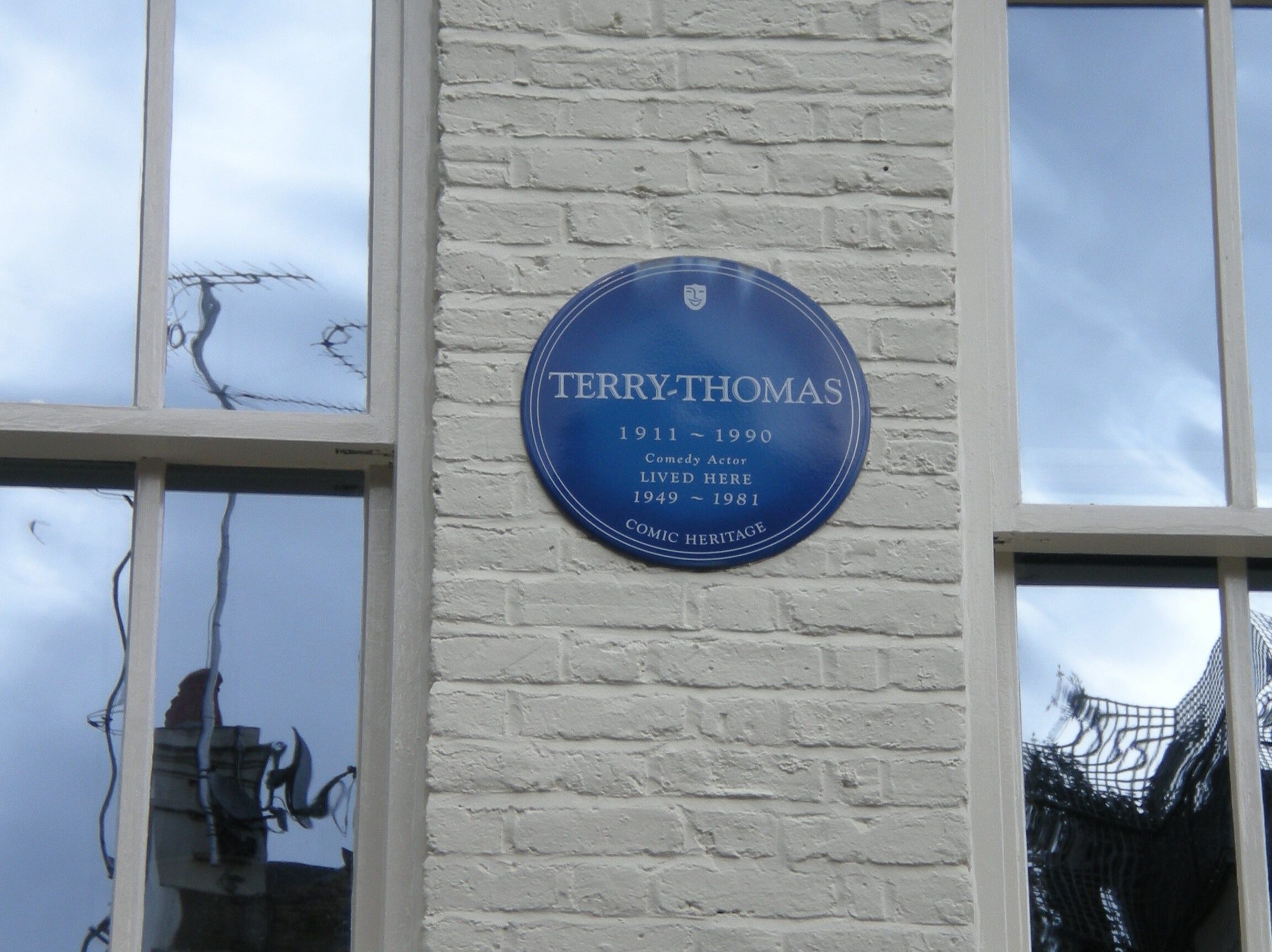 Blue commemorative plaques for Terry-Thomas on a white brick building.